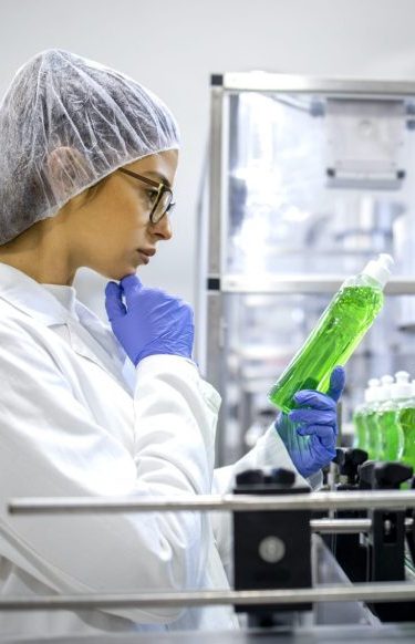 Female technologist controlling production of cleaning supplies or sanitation chemicals for cleaning industry. Checking quality of detergent.