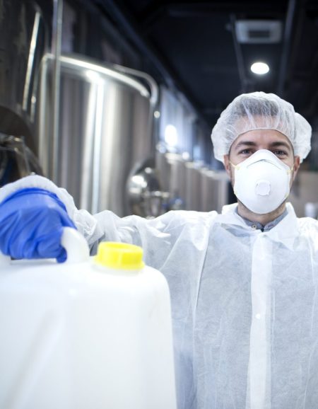 Industrial worker with protective mask and white uniform holding plastic cans for chemical industry.